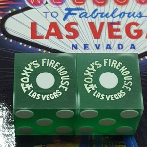 May include: Two green dice with white spots and the words "Today's Firehouse Las Vegas" printed on each side.