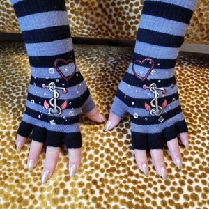 May include: A pair of fingerless gloves with a black and gray striped pattern. The gloves have a red heart and an anchor design with rhinestones.