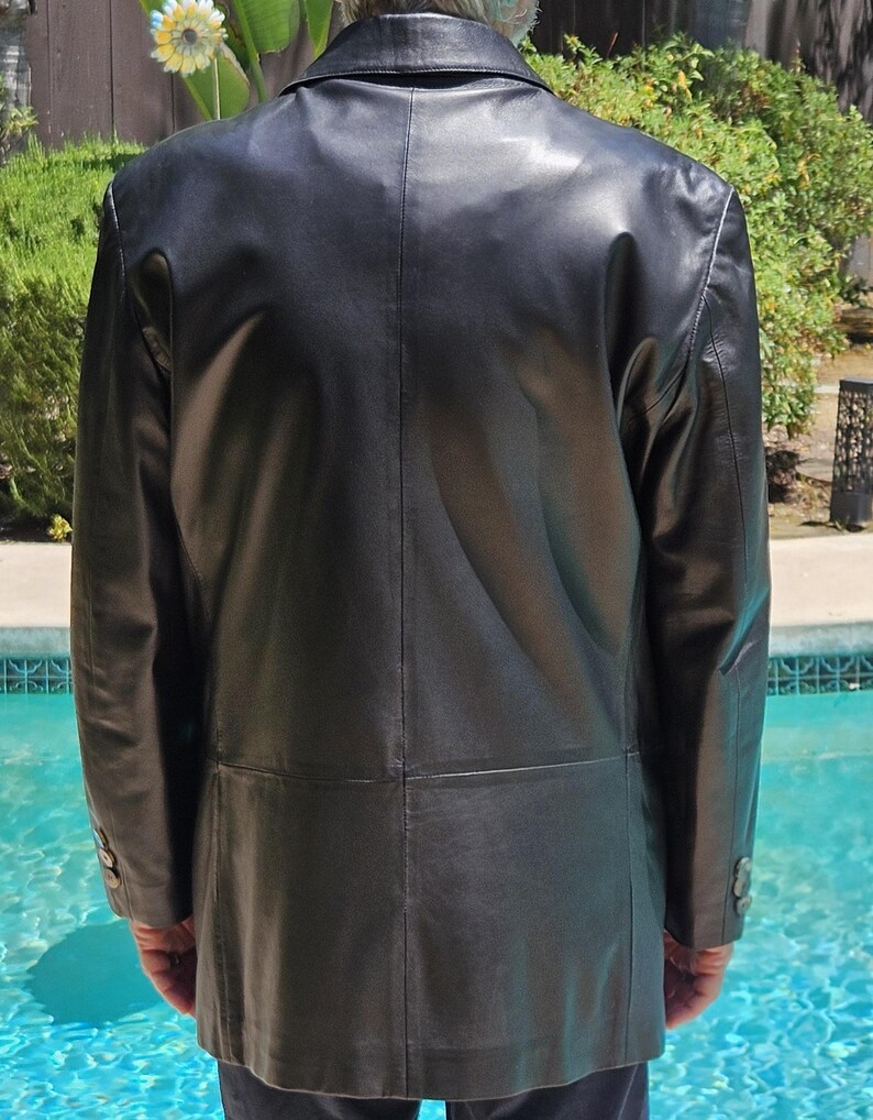 Pu&ograve; includere: Un blazer in pelle nera caratterizzato da un classico colletto a revers, maniche lunghe con tre bottoni su ogni polsino e una cucitura orizzontale sulla parte bassa della schiena. La giacca presenta una finitura liscia e una linea strutturata.