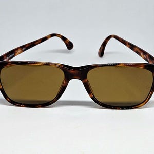 May include: Tortoiseshell-patterned sunglasses with brown lenses and gold-tone accents at the hinges. The inner temple arm is inscribed with Giorgio Armani Made in Italy, and the right lens features a small GA logo in the corner.