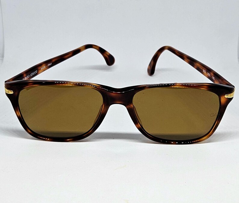 May include: Tortoiseshell-patterned sunglasses with brown lenses and gold-tone accents at the hinges. The inner temple arm is inscribed with Giorgio Armani Made in Italy, and the right lens features a small GA logo in the corner.