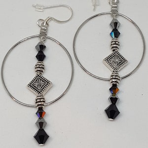 May include: Silver hoop earrings with black crystal beads and a silver charm. The charm is a square with a decorative design.