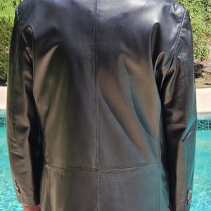 Pu&ograve; includere: Un blazer in pelle nera con colletto classico, maniche lunghe con tre bottoni su ogni polsino e una cucitura centrale sul retro. La giacca presenta una finitura liscia e un taglio strutturato che arriva fino ai fianchi con una cucitura orizzontale posteriore.