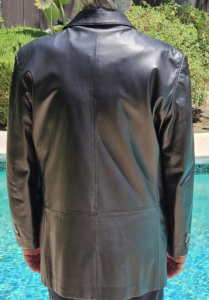Pu&ograve; includere: Un blazer in pelle nera con colletto classico, maniche lunghe con tre bottoni su ogni polsino e una cucitura centrale sul retro. La giacca presenta una finitura liscia e un taglio strutturato che arriva fino ai fianchi con una cucitura orizzontale posteriore.