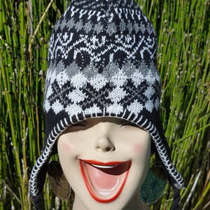 May include: Black and white knit beanie with a pom pom on top. The beanie has a geometric pattern and long black tassels.