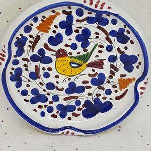May include: A white ceramic coaster with a blue, brown, and orange floral design and a yellow bird with green and red accents.