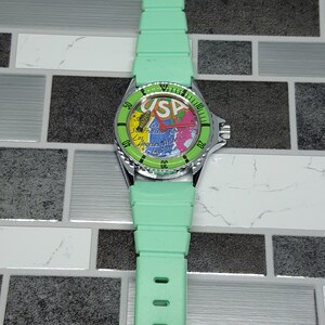 May include: A green wristwatch with a silver band and a map of the USA on the face. The watch face also has the text "USA" on it.