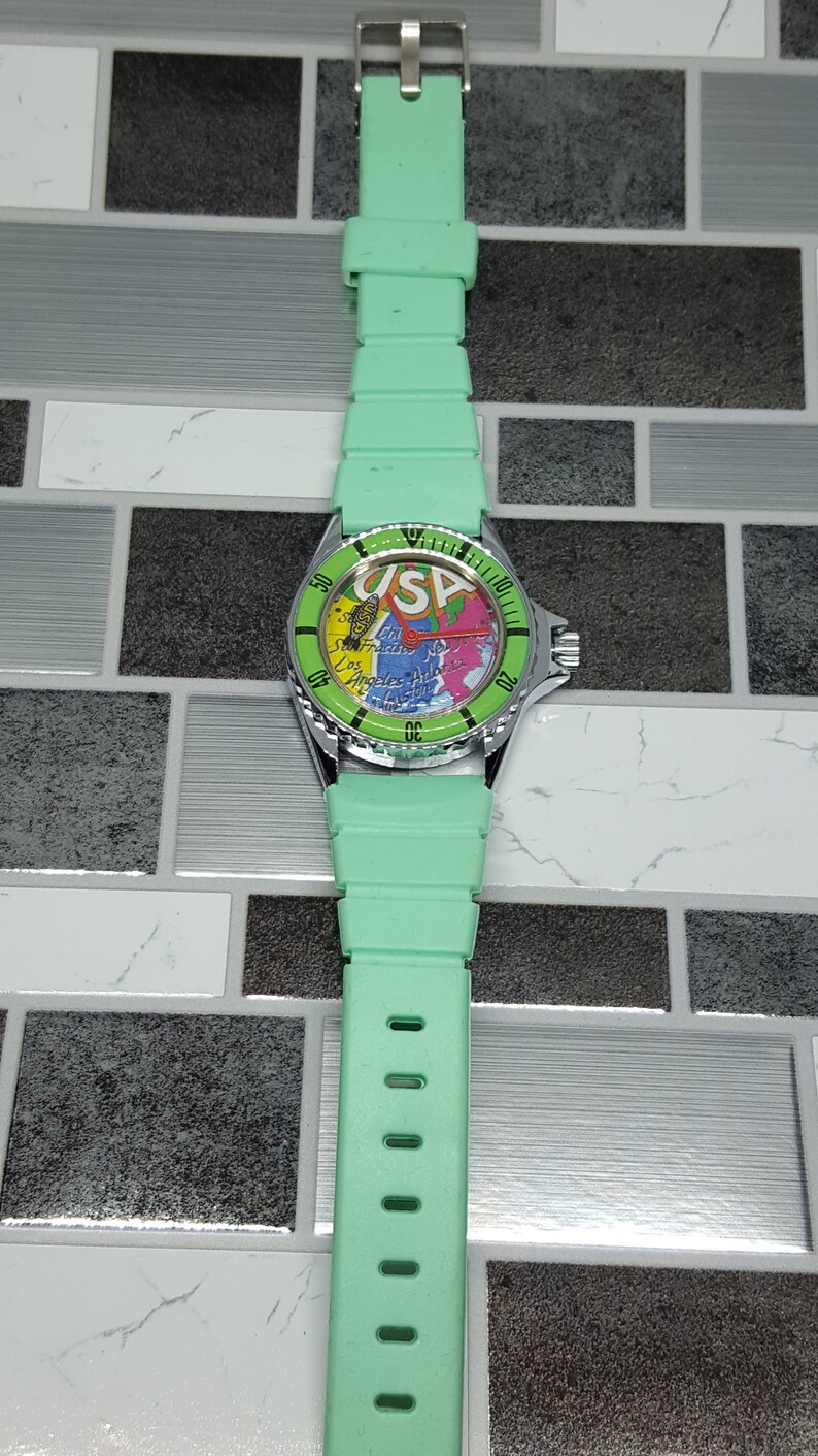 May include: A green wristwatch with a silver band and a map of the USA on the face. The watch face also has the text "USA" on it.