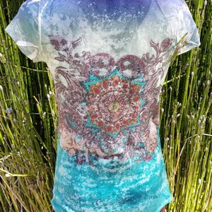 May include: A sheer white t-shirt with a blue, turquoise, and green ombre design. The shirt features a large, colorful mandala print in the center.