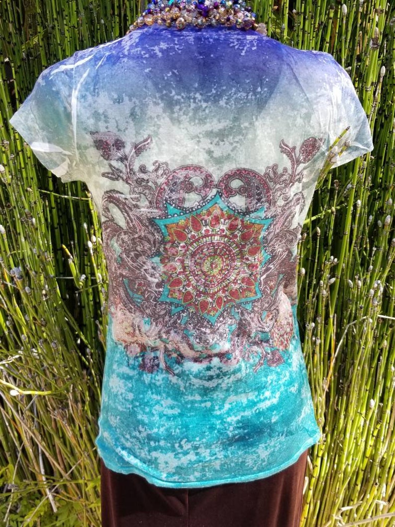 May include: A sheer white t-shirt with a blue, turquoise, and green ombre design. The shirt features a large, colorful mandala print in the center.