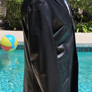 Pu&ograve; includere: Un blazer in pelle nera con revers dentellato, chiusura frontale a petto singolo e tre piccoli bottoni su ciascun polsino della manica. La giacca presenta una finitura liscia e lucida e una vestibilit&agrave; strutturata, vista di profilo.