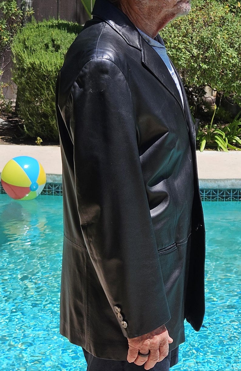 Pu&ograve; includere: Un blazer in pelle nera con revers dentellato, chiusura frontale a petto singolo e tre piccoli bottoni su ciascun polsino della manica. La giacca presenta una finitura liscia e lucida e una vestibilit&agrave; strutturata, vista di profilo.