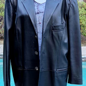 Pu&ograve; includere: Un blazer in pelle nera con revers dentellato, tre bottoni frontali e una tasca sul petto. Il blazer &egrave; indossato sopra un top viola chiaro con un motivo sottile e una collana color argento con un ciondolo a forma di teschio.