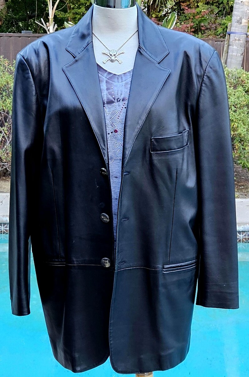 Pu&ograve; includere: Un blazer in pelle nera con revers dentellato, tre bottoni frontali e una tasca sul petto. Il blazer &egrave; indossato sopra un top viola chiaro con un motivo sottile e una collana color argento con un ciondolo a forma di teschio.