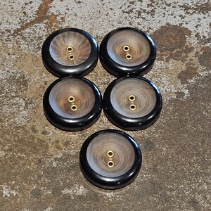 May include: Six round wooden buttons with a black rim and two gold metal holes. The buttons have a wood grain pattern.