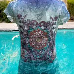 May include: A turquoise blue, white, and purple short-sleeved shirt with a mandala design. The shirt has a faded, distressed look.
