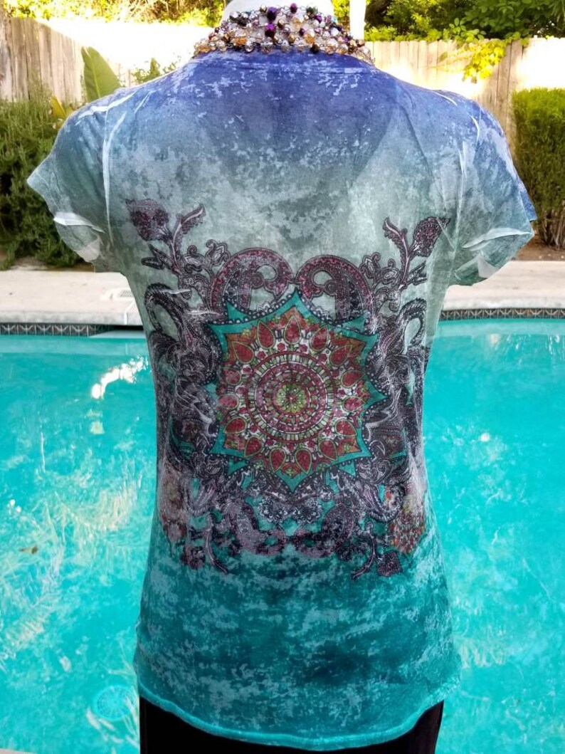 May include: A turquoise blue, white, and purple short-sleeved shirt with a mandala design. The shirt has a faded, distressed look.