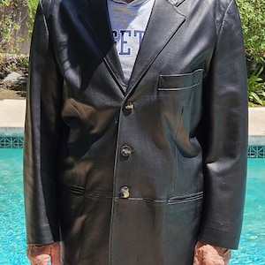 Pu&ograve; includere: Un blazer in pelle nera con revers dentellato, tre bottoni frontali e una tasca sul petto. La giacca &egrave; indossata sopra una felpa grigia con cappuccio con il testo parziale "ET" visibile sul davanti, caratterizzata da un design strutturato.