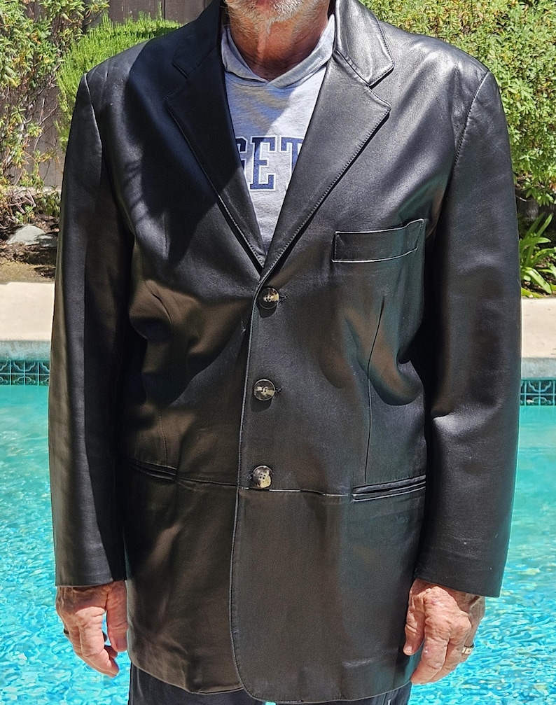 Pu&ograve; includere: Un blazer in pelle nera con revers dentellato, tre bottoni frontali e una tasca sul petto. La giacca &egrave; indossata sopra una felpa grigia con cappuccio con il testo parziale "ET" visibile sul davanti, caratterizzata da un design strutturato.