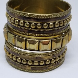 May include: A set of four gold-toned bangles with intricate designs. The bangles feature a combination of smooth, beaded, and textured surfaces.