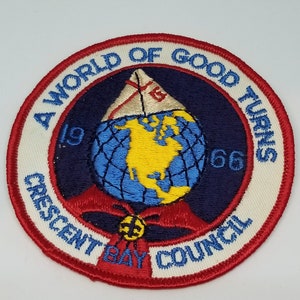 May include: A blue and white embroidered patch with a red border. The patch features a globe with a sailboat on top, a yellow bug, and the text "A World of Good Turns 1966 Crescent Bay Council".