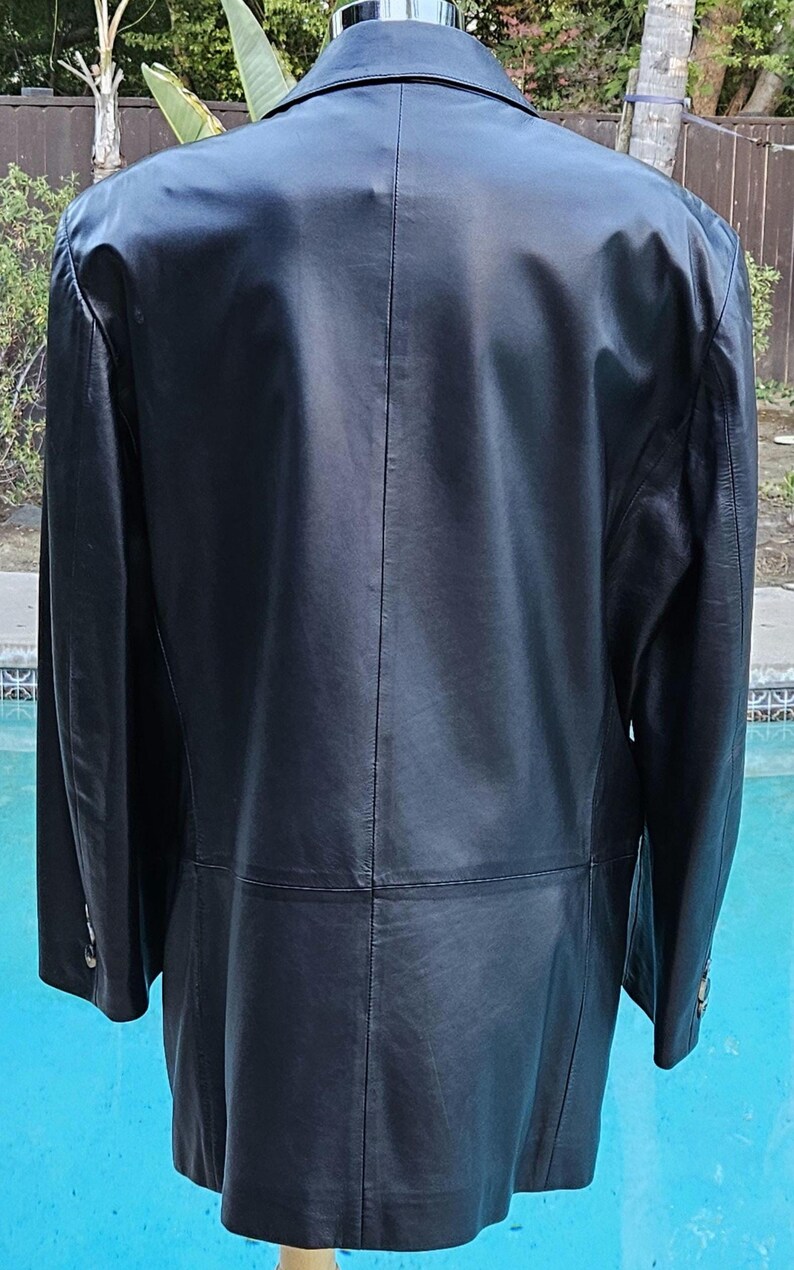 Pu&ograve; includere: Un blazer in pelle nera con colletto classico, maniche lunghe con polsini abbottonati e una cucitura verticale che corre lungo il centro della schiena. La giacca ha una finitura liscia e un orlo dritto, offrendo un aspetto strutturato.