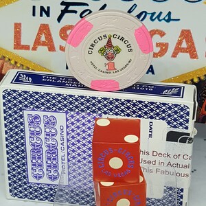 May include: A pink and white casino chip with the text "Circus Circus Hotel/Casino/Las Vegas, NV" and a clown illustration. Two red dice with white dots and the text "Circus Circus Las Vegas" are on a blue and white card with the text "Circus Circus Hotel/Casino".