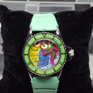 May include: A green wristwatch with a map of the USA on the face. The watch has a silver bezel with black markings and a green strap.