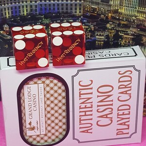 May include: Two red dice with white dots and the text "Hyatt Regency" on each side. The dice are sitting on top of a white box with the text "Authentic Casino Played Cards" and "Grand Lodge Casino at Hyatt Regency Lake Tahoe".