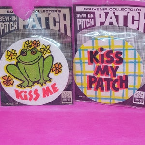 May include: Two sew-on patches, one with a green frog and the text "Kiss Me" and the other with a plaid background and the text "Kiss My Patch".