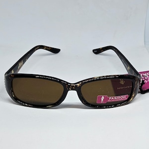 May include: Tortoise shell sunglasses with brown lenses. The sunglasses have a small, pink tag that says "FASHION 100% UV-OVER PROTECTION".