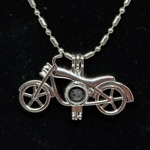 May include: Silver motorcycle charm necklace with a ball chain. The charm is open and has a small, round, black stone inside.