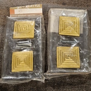 May include: Two sets of gold-colored square cabinet knobs with concentric circles. Each set comes with two knobs and two screws.