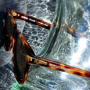 May include: Tortoiseshell-patterned sunglasses with dark lenses and gold-tone metal accents. The inner temple arm features the text Giorgio Armani and Made in Italy, while the outer temple arm displays the Giorgio Armani brand name in gold lettering.
