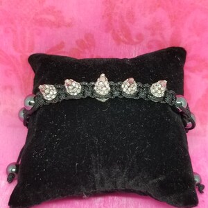 May include: Black bracelet with silver spikes and black beads. The bracelet is on a black velvet pillow.