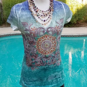 May include: A teal blue, green, and purple t-shirt with a beaded design and a multi-strand beaded necklace.