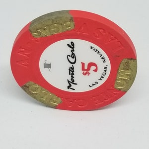 May include: Red and gold casino chip with the text "Monte Carlo" and "$5 LAS VEGAS, NEVADA" on it.