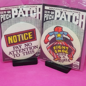 May include: Two sew-on patches. The first patch is white with black text that says "NOTICE PAY NO ATTENTION TO THIS." The second patch is white with a cartoon illustration of a person riding a horse. The text on the second patch says "FIGHT SMOG RIDE A HORSE".