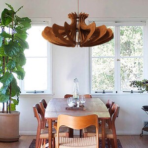 May include: A wooden ceiling light fixture with a unique, modern design hangs over a dining table with six chairs. The light fixture is made of multiple layers of wood that are arranged in a spiral pattern. The table is made of wood and has a light brown finish. The chairs are also made of wood and have a dark brown finish.