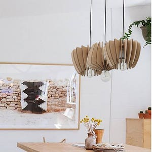 May include: A wooden pendant light fixture with a unique, geometric design. The light fixture is made of multiple thin pieces of wood that are arranged in a fan-like pattern. The light fixture is hanging from the ceiling and is illuminating a dining room table.