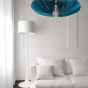 May include: A teal blue wooden ceiling light fixture with a modern design hangs over a white couch with white pillows in a living room.