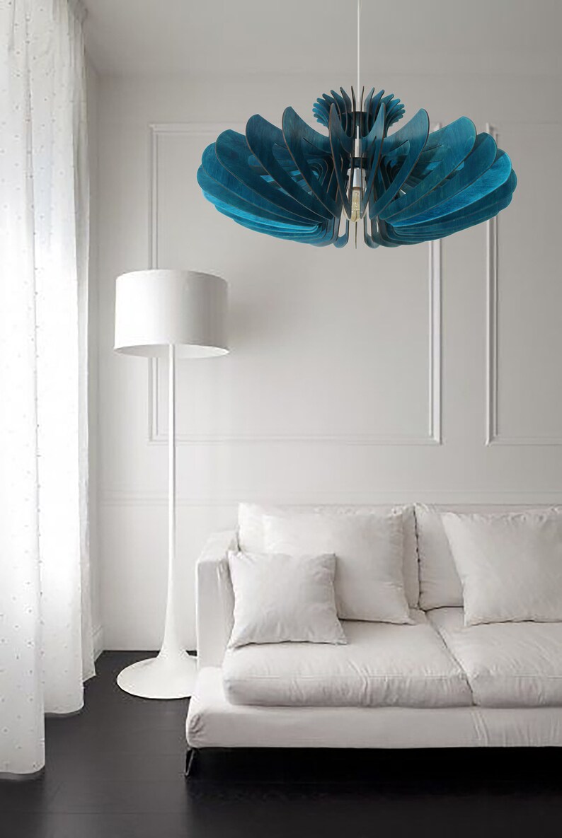 May include: A teal blue wooden ceiling light fixture with a modern design hangs over a white couch with white pillows in a living room.
