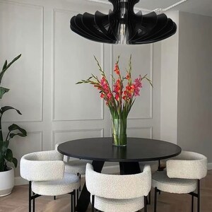 May include: A black modern dining table set with four white chairs. The table has a round top and a black base. The chairs have a white fluffy fabric seat and back with black metal legs. A black modern chandelier hangs above the table.