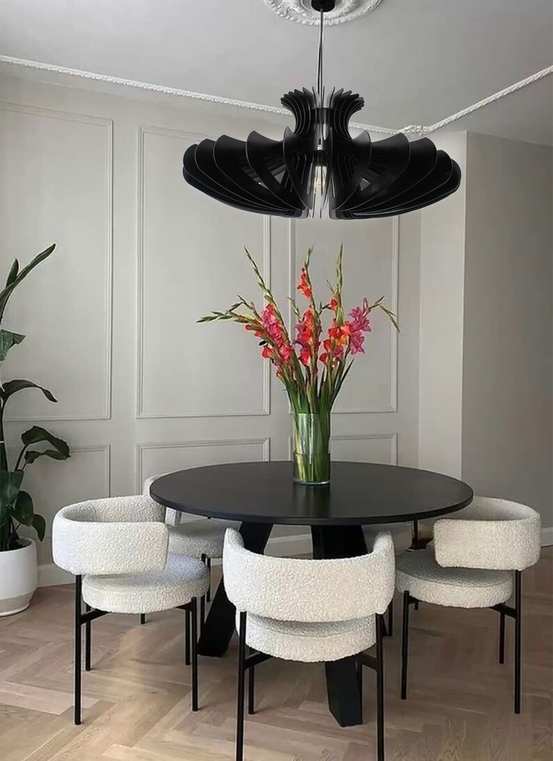 May include: A black modern dining table set with four white chairs. The table has a round top and a black base. The chairs have a white fluffy fabric seat and back with black metal legs. A black modern chandelier hangs above the table.