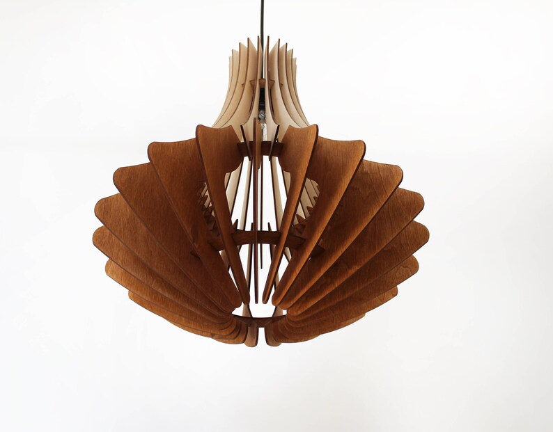 May include: A wooden pendant light fixture with a layered, fan-like design. The light fixture is made of light and dark brown wood, with a bulb visible inside. The fixture hangs from a black cord against a white background.