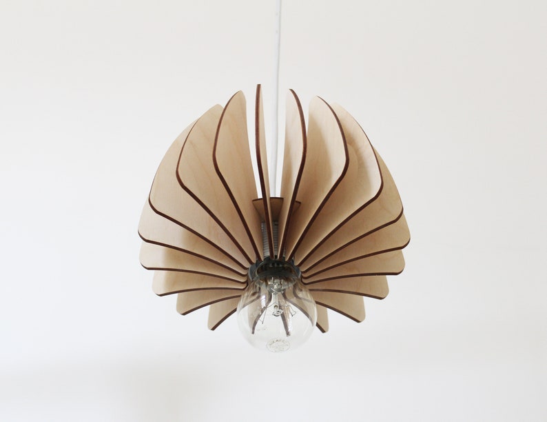 May include: A wooden pendant light fixture with a unique fan-shaped design. The light fixture is made of thin, light wood slats that are arranged in a circular pattern. The light fixture is suspended from the ceiling by a single cord.