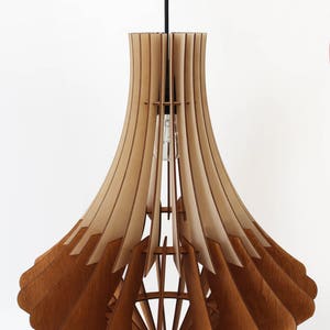 May include: A wooden pendant light fixture with a layered, fan-like design. The light fixture is made of light and dark brown wood, with a bulb visible inside. The fixture hangs from a black cord against a white background.