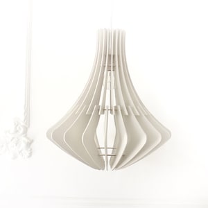 May include: A modern, white pendant light fixture with a layered, geometric design. The light has a flared, bell-like shape, with vertical slats creating a unique pattern. The fixture hangs from a white cord against a white wall.