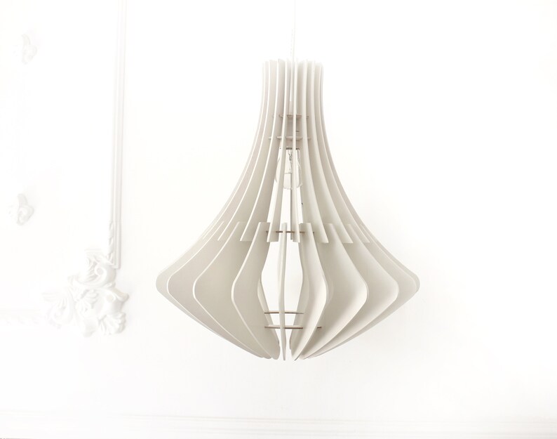 May include: A modern, white pendant light fixture with a layered, geometric design. The light has a flared, bell-like shape, with vertical slats creating a unique pattern. The fixture hangs from a white cord against a white wall.