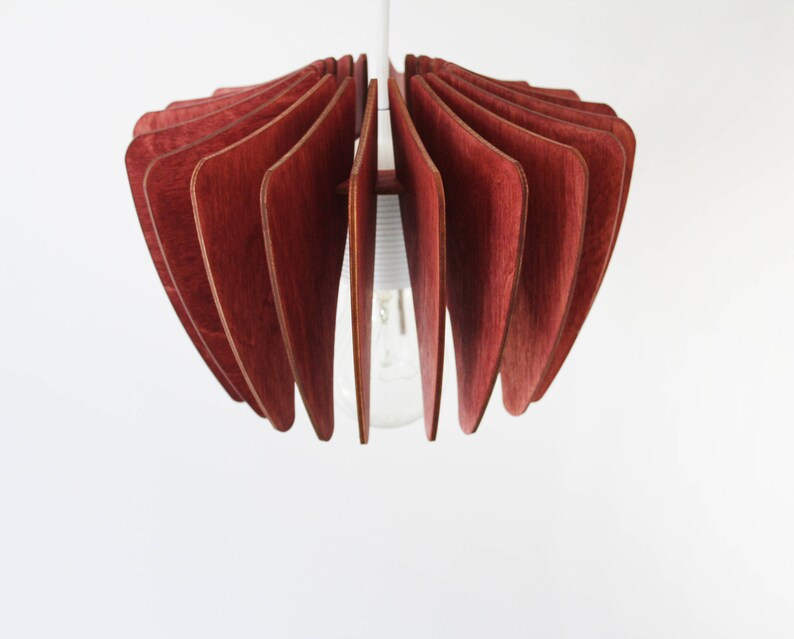 May include: A red wooden pendant light fixture with a unique, geometric design. The light fixture is made of thin, curved pieces of wood that are arranged in a fan shape. The light fixture is suspended from the ceiling by a single cord.
